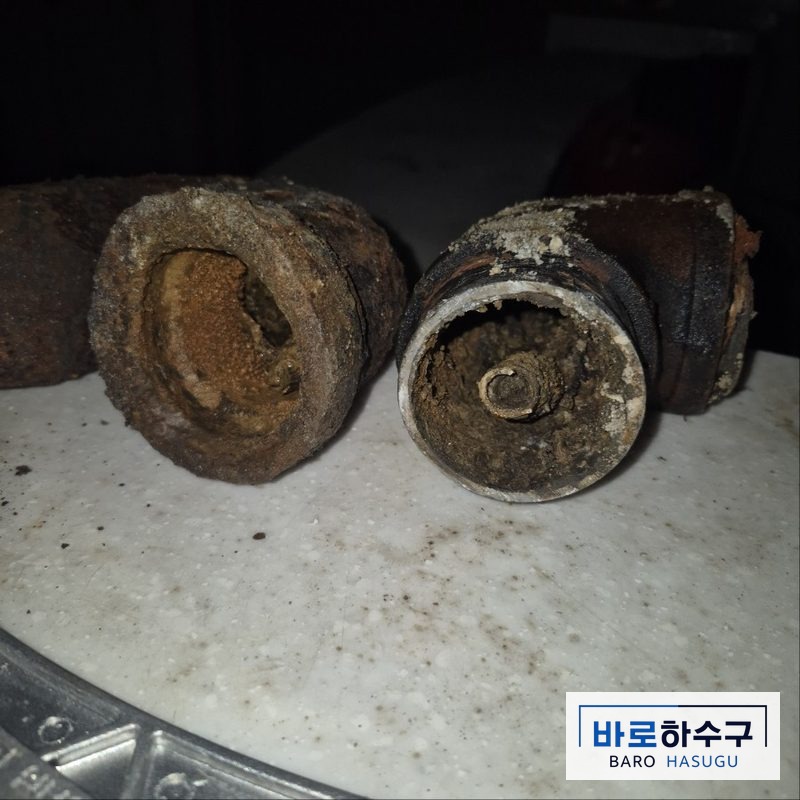 배관막힘 작업 전, 바닥에서 걷어낸 주철 배관 단면에 녹과 찌꺼기가 두껍게 덮인 상태 (군포 현장)